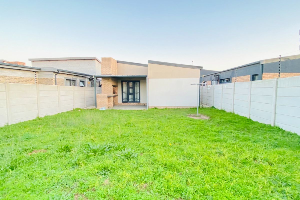 Rear view of the property featuring a private garden, enclosed by precast concrete walls with electric fencing, and a built-in brick braai area.
