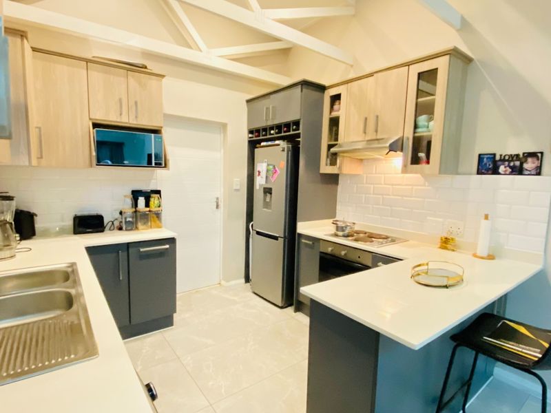 Modern kitchen featuring two-tone cabinetry, stone countertops, subway tile backsplash, and exposed ceiling beams, offering a functional and stylish cooking space.