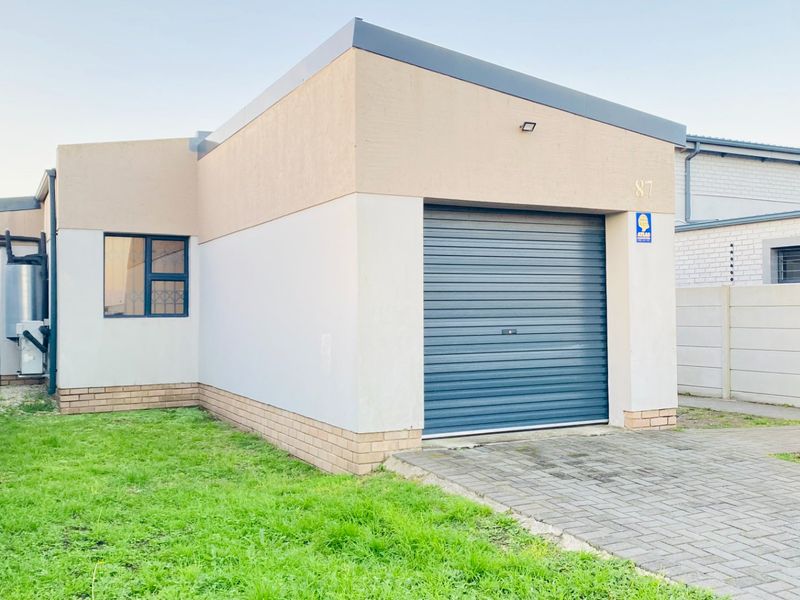 Front view of a modern house featuring a single roller garage door, paved driveway, and secure boundary wall with electric fencing.