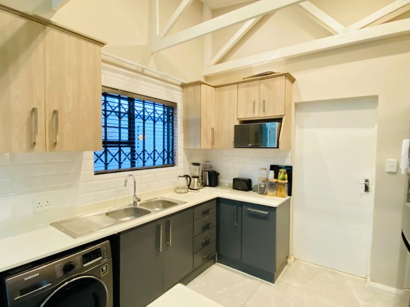 Modern kitchen featuring two-tone cabinetry, subway tile backsplash, double sink, and exposed roof trusses, providing a bright and functional workspace.