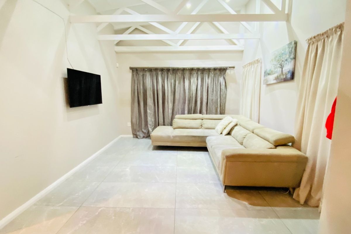 A spacious living room featuring high ceilings with exposed white trusses and large format floor tiles, creating a bright and airy atmosphere.