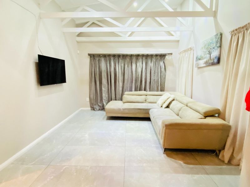 A spacious living room featuring high ceilings with exposed white trusses and large format floor tiles, creating a bright and airy atmosphere.