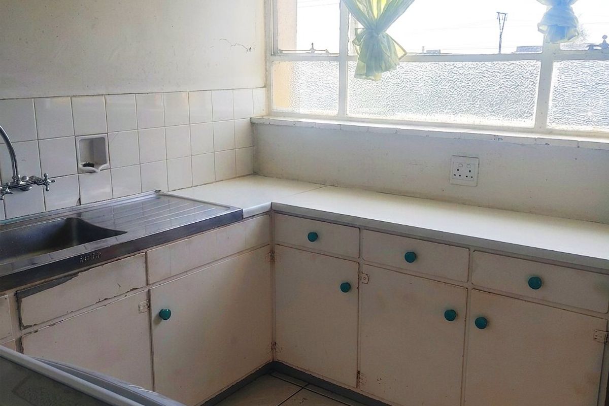 A dated kitchen featuring original cabinetry, tiled backsplash, and a stainless steel sink, offering significant potential for modernization and renovation.