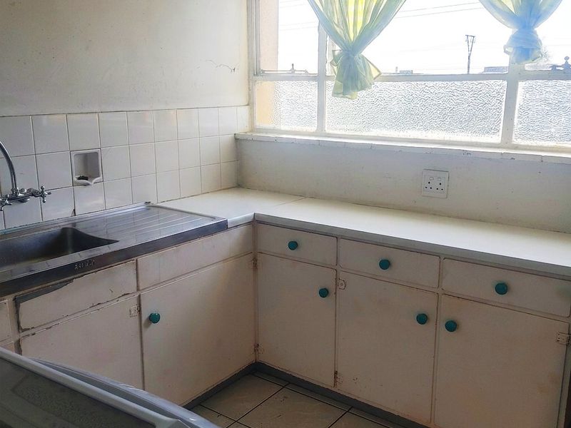 A dated kitchen featuring original cabinetry, tiled backsplash, and a stainless steel sink, offering significant potential for modernization and renovation.