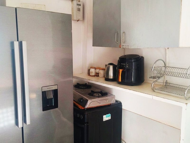 A compact kitchen area featuring wall-mounted cabinetry, open shelving, and an electrical distribution board, requiring cosmetic updates to improve functionality and aesthetic appeal.