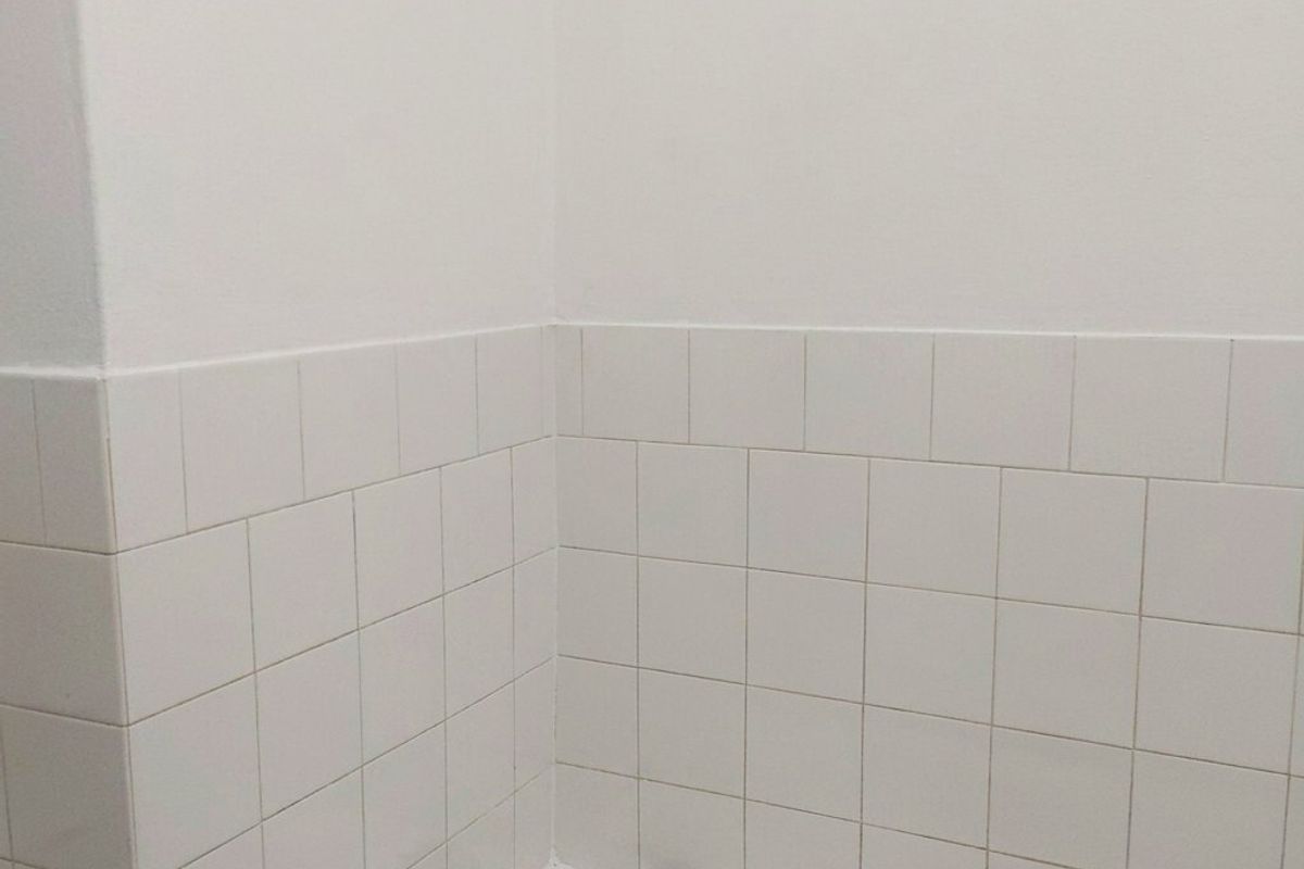 A clean, minimalist bathroom featuring a standard white bathtub with chrome faucets and white wall tiling.