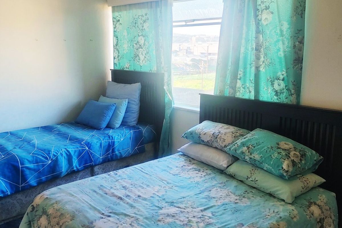 A bedroom featuring a sliding window with a ventilation grille, showing signs of wear on the wall surfaces.