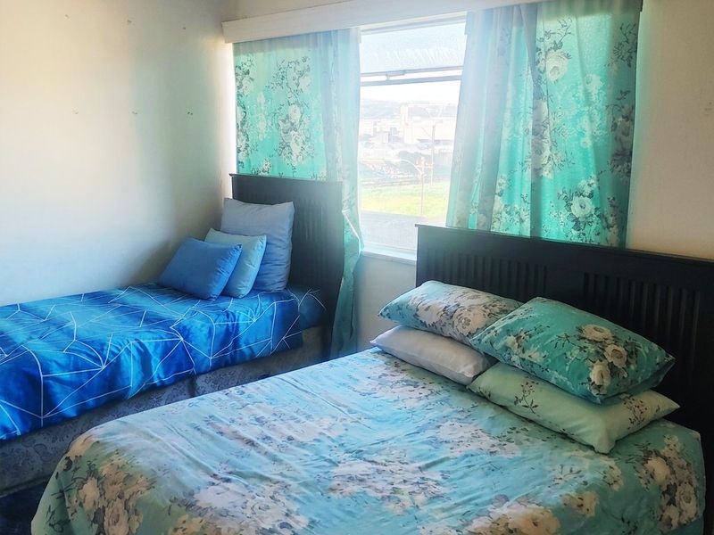 A bedroom featuring a sliding window with a ventilation grille, showing signs of wear on the wall surfaces.