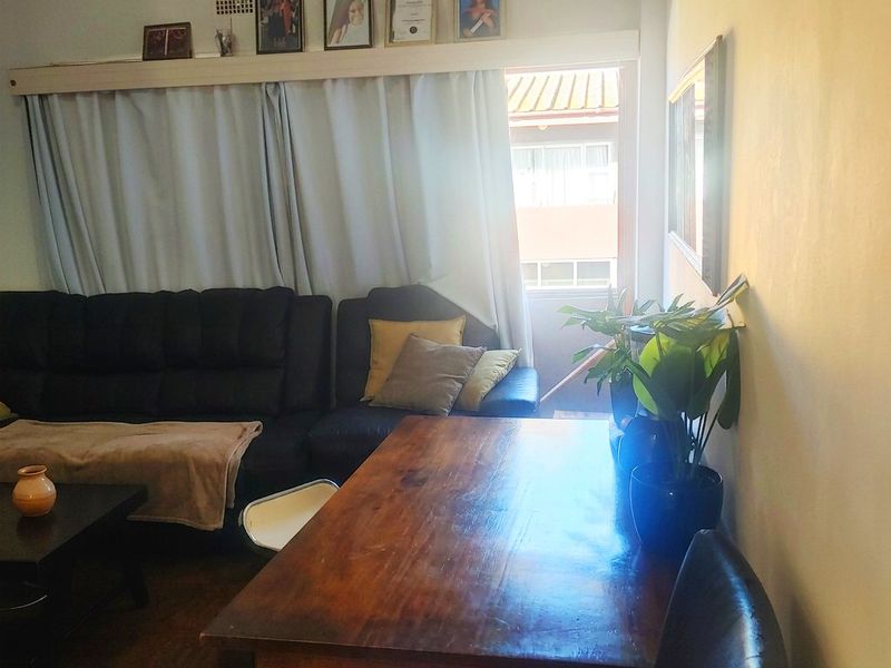 A living room area featuring a curtained window and ventilation grille, with a view towards an adjacent building exterior.