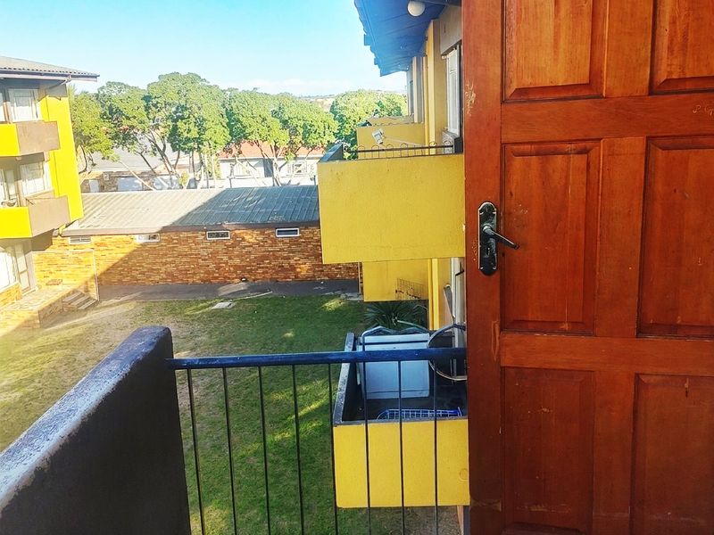 A view from an apartment balcony overlooking the complex grounds, featuring a metal balustrade and a wooden entrance door.