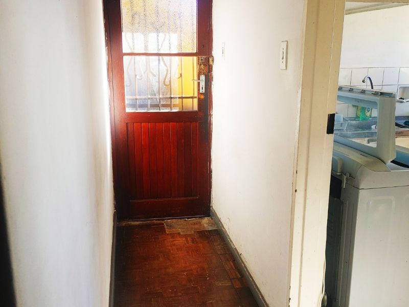 An entry hallway featuring traditional parquet flooring and a timber door with a security gate, leading into an adjacent utility area.