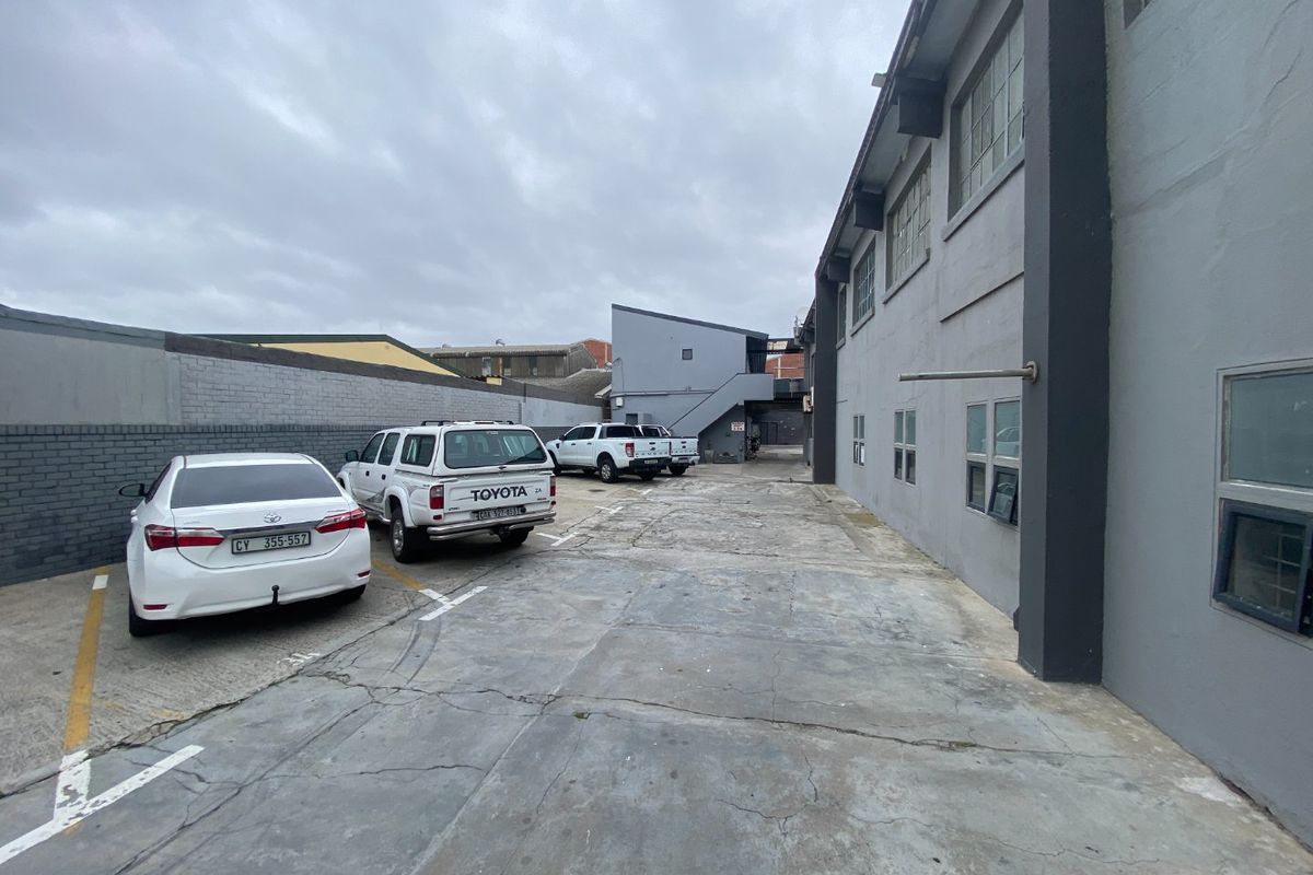Rear exterior view of a commercial property featuring a concrete paved parking area, boundary wall, and external staircase access.