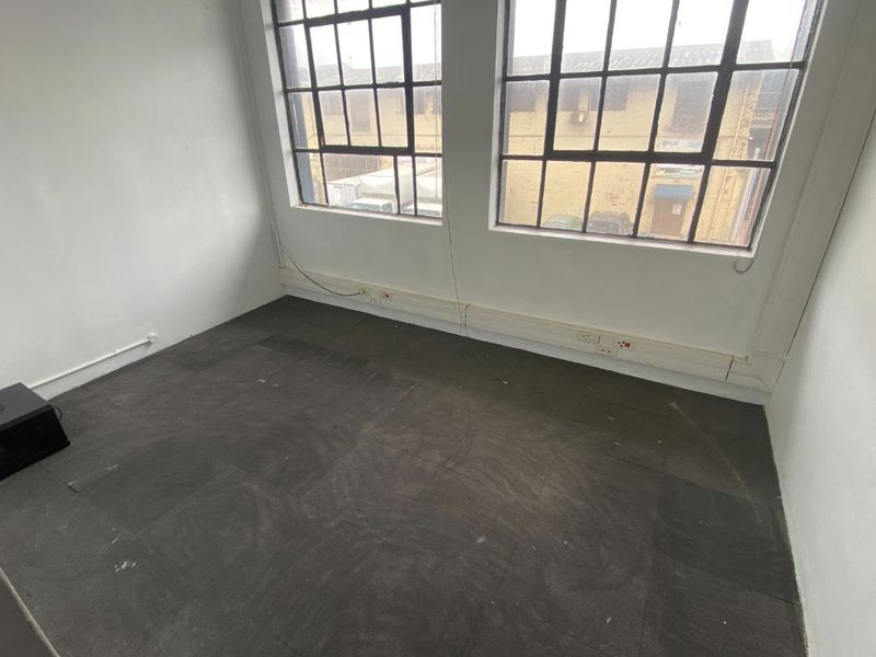An empty office space featuring industrial-style steel-framed windows, surface-mounted electrical trunking, and carpet tile flooring, ready for refurbishment.
