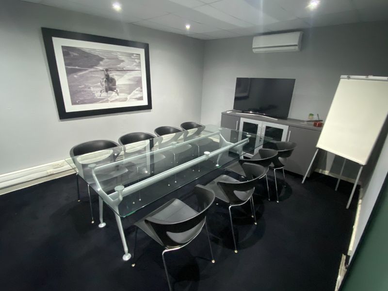 A professional meeting room featuring a glass conference table, wall-mounted air conditioning, and built-in storage cabinetry.