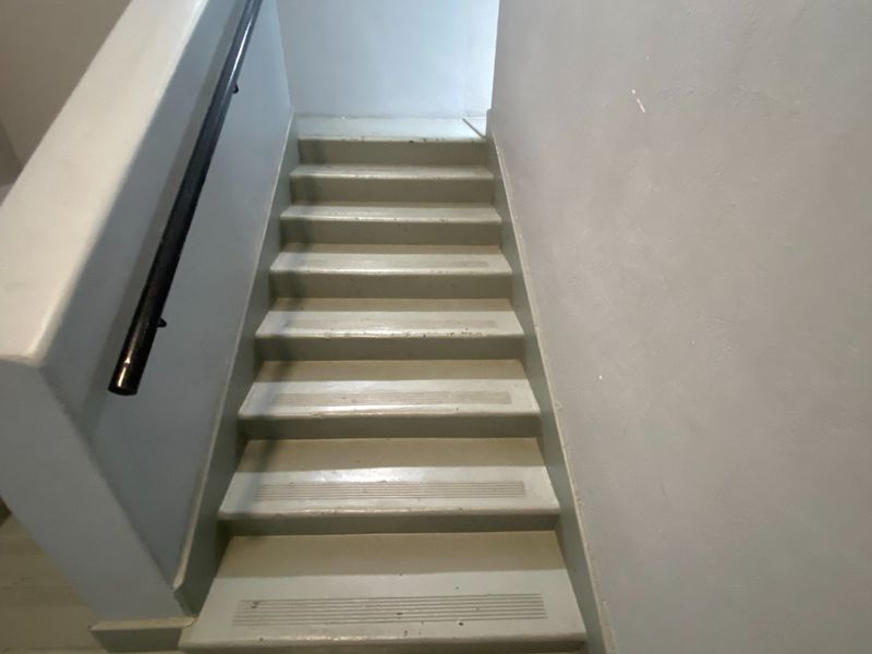 A functional interior staircase featuring a painted finish and a fixed handrail, showing signs of wear on the treads and walls.