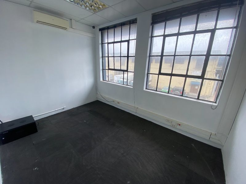 Empty office space featuring industrial-style steel-framed windows, grid ceiling, split-system air conditioning, and surface-mounted electrical trunking.