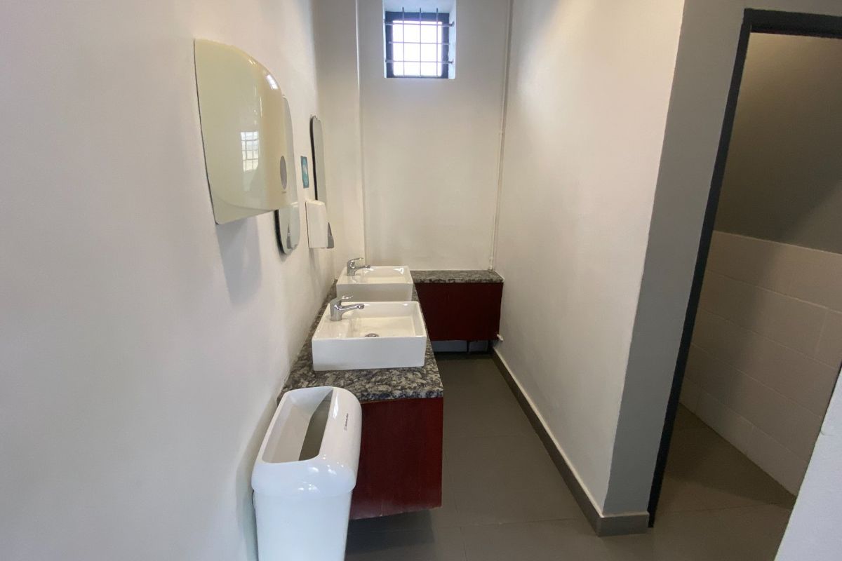 A functional commercial bathroom featuring a dual vanity setup with granite countertops, built-in cabinetry, and a secure window.