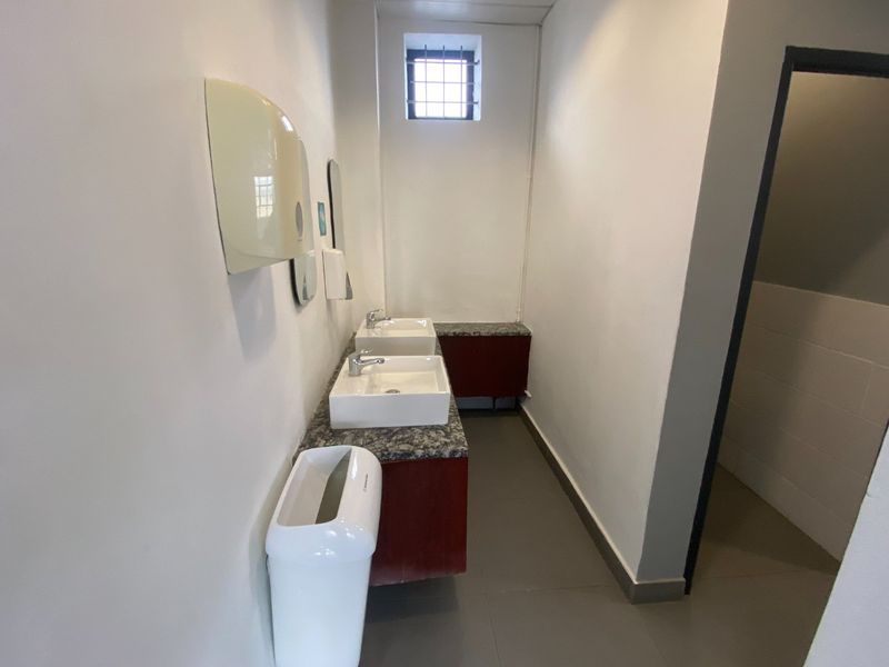 A functional commercial bathroom featuring a dual vanity setup with granite countertops, built-in cabinetry, and a secure window.