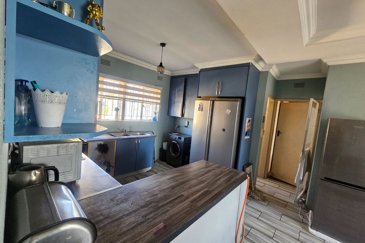 A functional kitchen featuring blue cabinetry, a wood-look laminate countertop, double sink, and tiled flooring, requiring some cosmetic updates to the cabinetry.