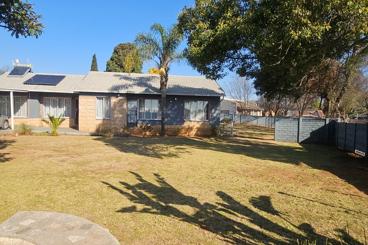 Rear view of the property featuring a spacious lawn, solar water heating system, and secure boundary walling.