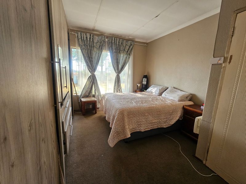 A bedroom featuring built-in wardrobes and carpeted flooring, showing signs of wear including ceiling cracks and damaged door frame finishes.