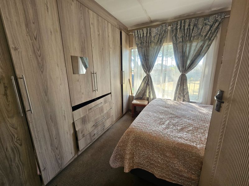 A bedroom featuring extensive built-in wooden cupboards and a window with security bars, showing signs of wear on the cabinetry and ceiling.