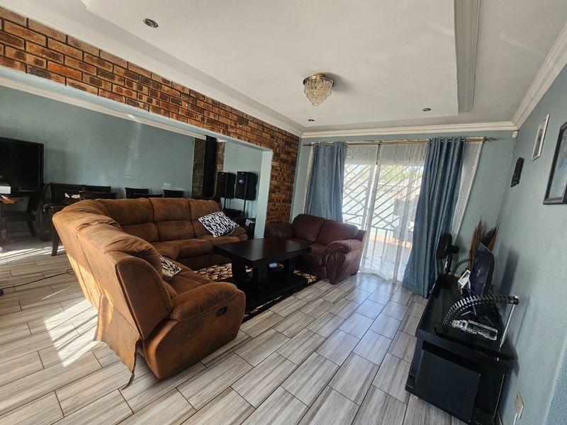 A spacious living room featuring tiled flooring, an exposed brick accent wall, and a sliding glass door with security gate providing access to the exterior.