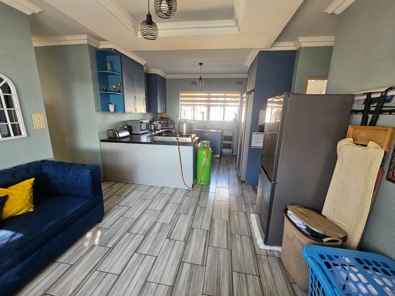 Open-plan kitchen and living area featuring modern wood-look tile flooring, blue cabinetry, and a tray ceiling with pendant lighting.
