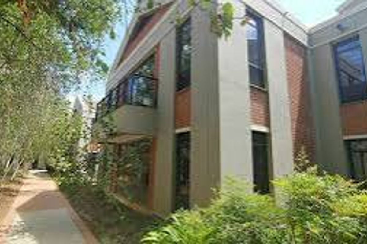 A view of the rear exterior of the commercial building, featuring a brick facade, a balcony, and a paved walkway through the garden.