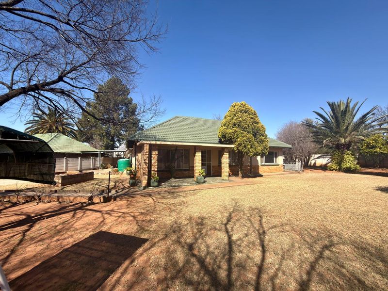 A view of the rear exterior of the house featuring a tiled roof, brick facade, and a covered patio area overlooking the garden.