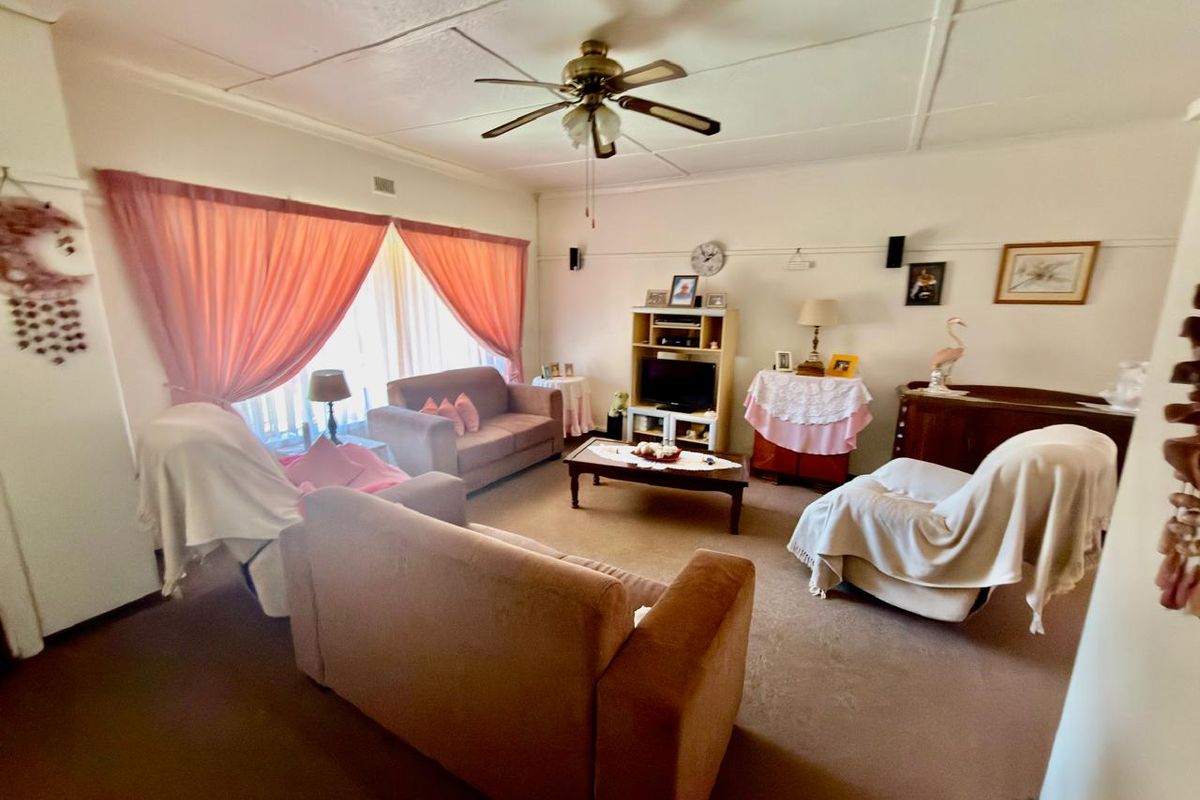A living room featuring a ceiling fan and traditional picture rails, showing signs of age and wear in the ceiling finishes.