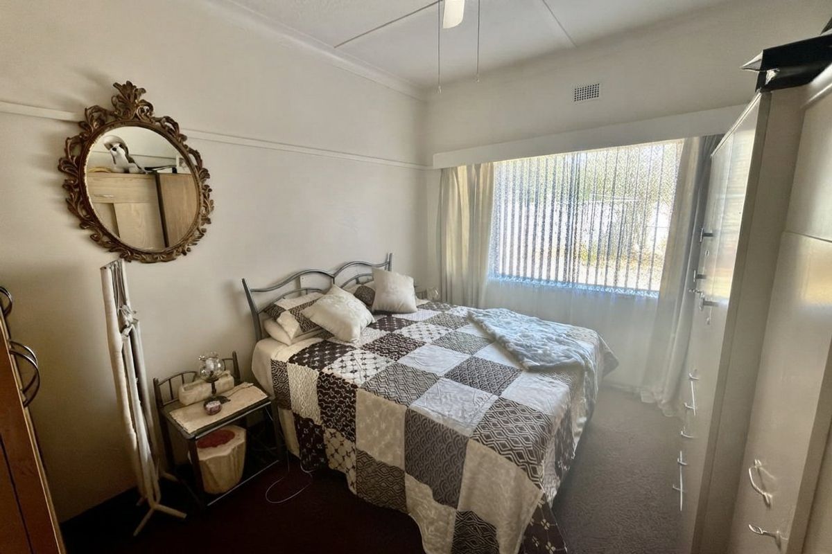 A functional bedroom featuring a ceiling fan, built-in wardrobe, and vertical blinds, providing a comfortable and practical living space.