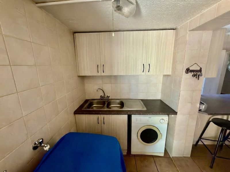 Compact laundry area featuring built-in cabinetry, a stainless steel sink, and dedicated space for a washing machine with tiled wall finishes.