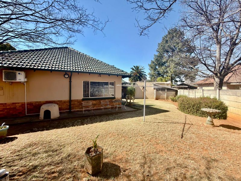 Rear view of the house featuring a tiled roof, brick perimeter wall, and a concrete patio area overlooking the garden.