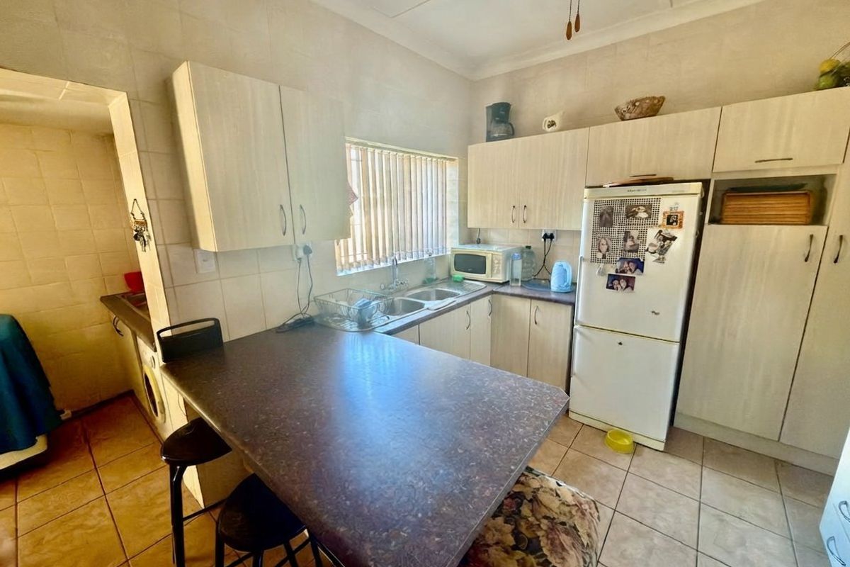 A functional kitchen featuring laminate cabinetry, a double basin sink, tiled flooring, and a built-in breakfast nook area.