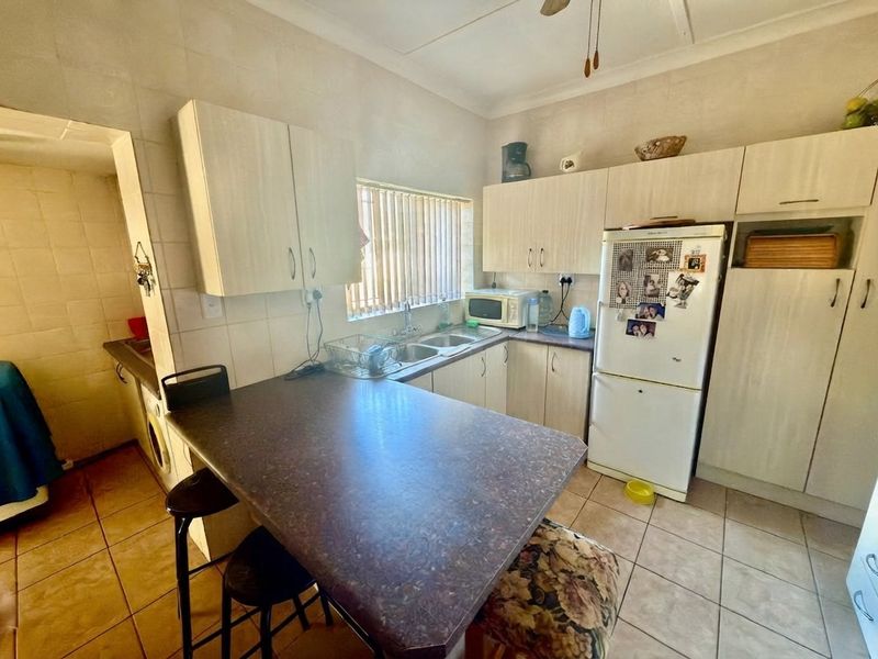 A functional kitchen featuring laminate cabinetry, a double basin sink, tiled flooring, and a built-in breakfast nook area.
