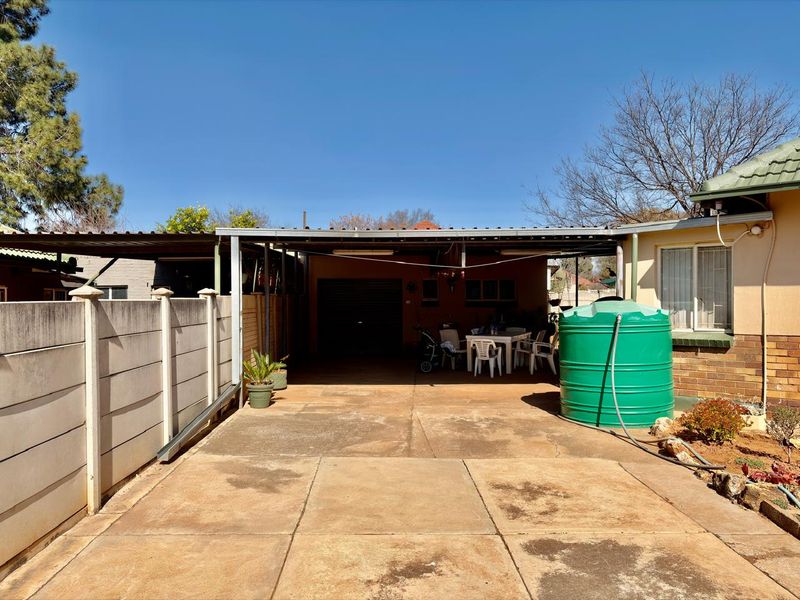 Rear exterior view featuring a covered carport, concrete driveway, and a large water storage tank adjacent to the main dwelling structure.