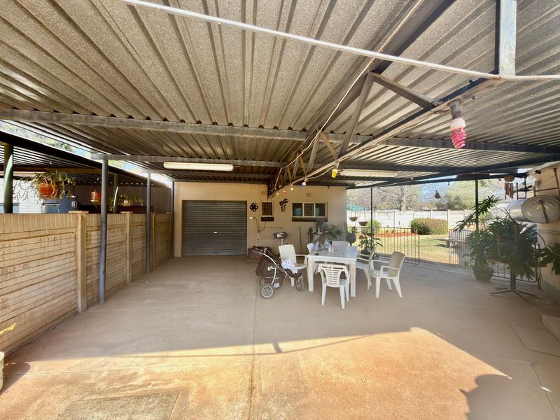 A spacious covered patio area featuring a corrugated metal roof, concrete flooring, and a built-in external sink, providing a functional outdoor entertainment space.