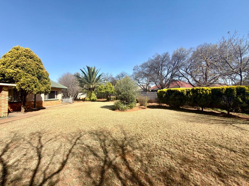 A spacious rear garden featuring a large lawn, established trees, and a brick-walled boundary, offering a private outdoor area.