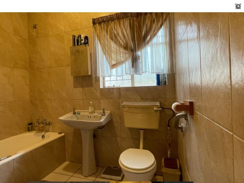 A functional bathroom featuring a bathtub, pedestal basin, and toilet with full-height wall tiling.