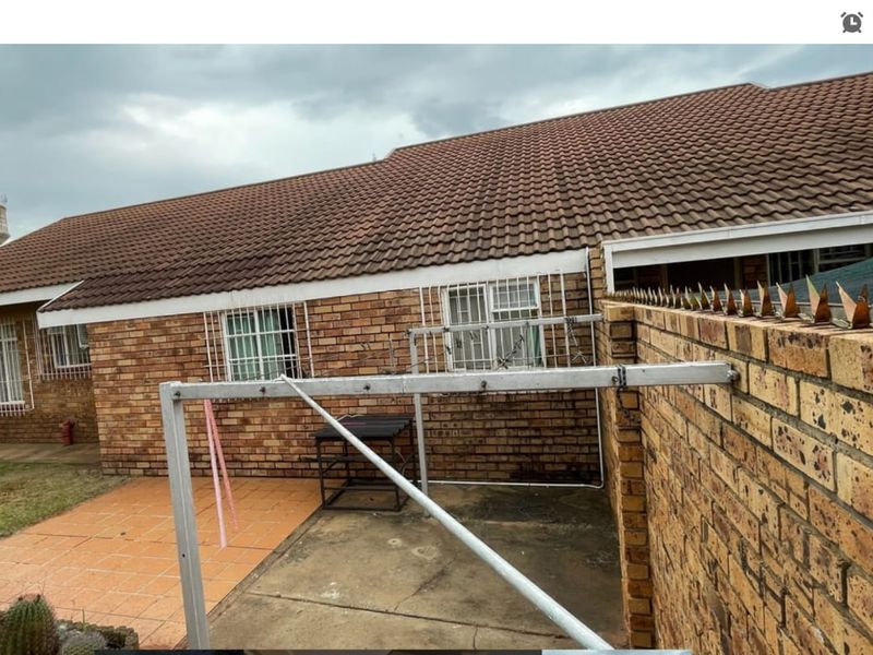 Rear exterior view of the apartment featuring a brick facade, tiled roof, paved patio area, and perimeter wall with security spikes.