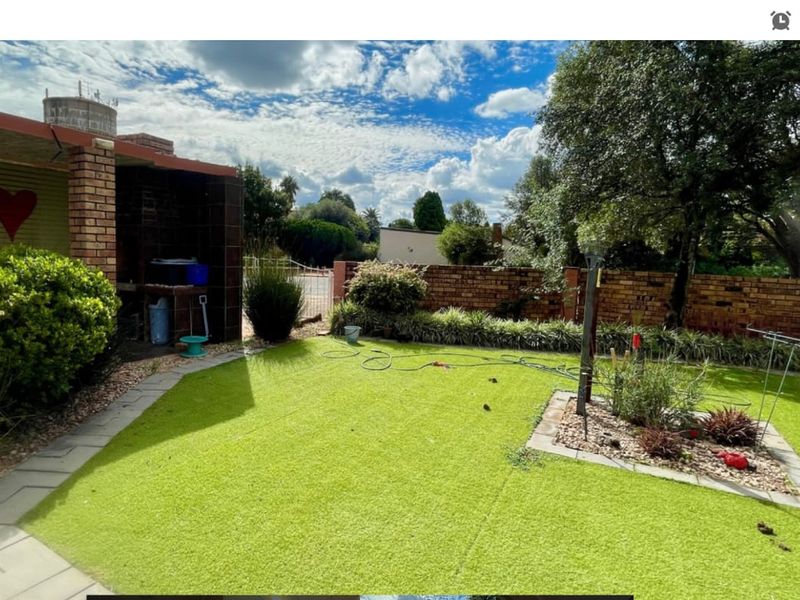 A rear garden area featuring a built-in brick braai, paved pathways, and a lawn enclosed by a brick boundary wall.