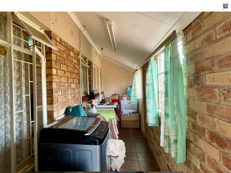 A functional laundry area featuring exposed brick walls, tiled flooring, and direct access to the exterior through a security gate.