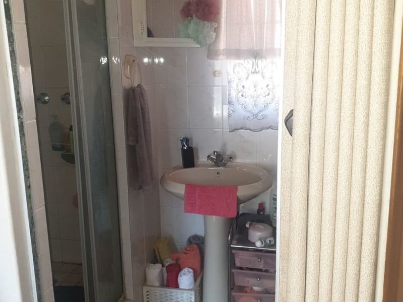 A compact bathroom featuring a pedestal basin, a shower enclosure, and tiled finishes, offering potential for a modern renovation.