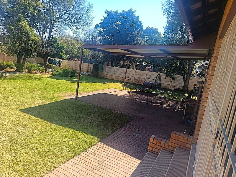 A spacious covered patio area featuring brick paving and steps, overlooking a large private garden with a perimeter wall.