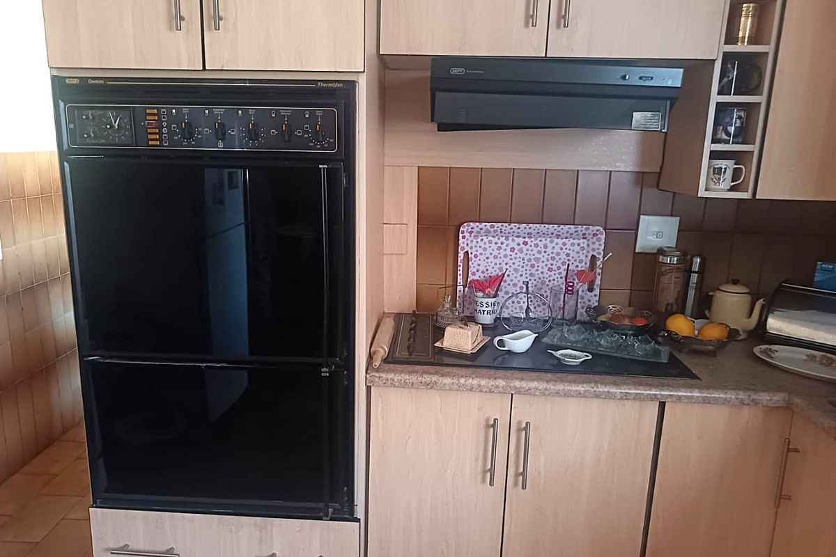 A functional kitchen featuring light wood-tone cabinetry, a built-in oven, an extractor fan, and a tiled backsplash with a laminate countertop.