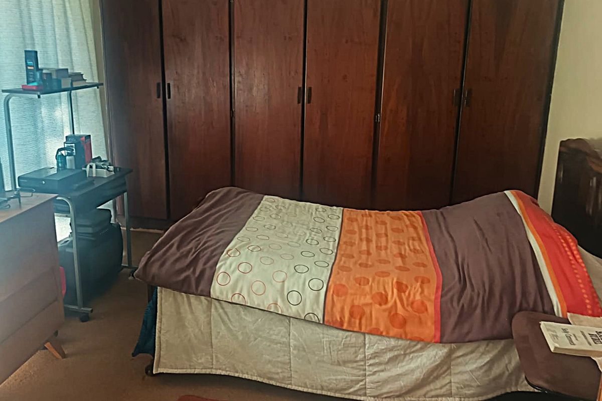 A bedroom featuring floor-to-ceiling wooden built-in cupboards and carpeted flooring.