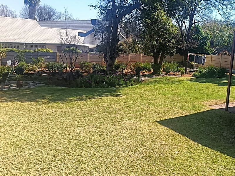 A well-maintained residential garden featuring a spacious lawn, mature trees, and secure boundary fencing.
