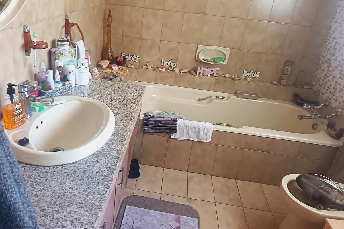 A functional bathroom featuring a built-in vanity with an integrated basin, a bathtub with tiled surround, and neutral wall and floor tiling.