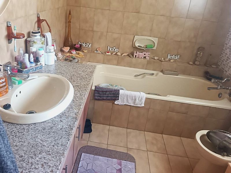 A functional bathroom featuring a built-in vanity with an integrated basin, a bathtub with tiled surround, and neutral wall and floor tiling.